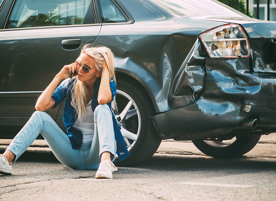 Report a Claim - Woman Sitting Down by Her Car After an Accident